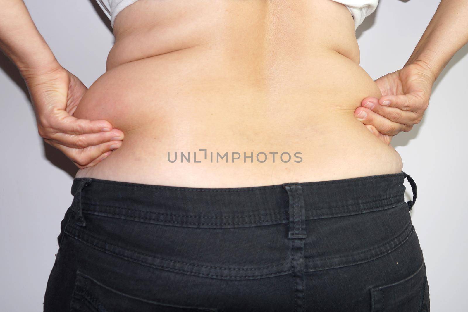 woman in jeans holds fat folds at her waist with her hands, rear view.
