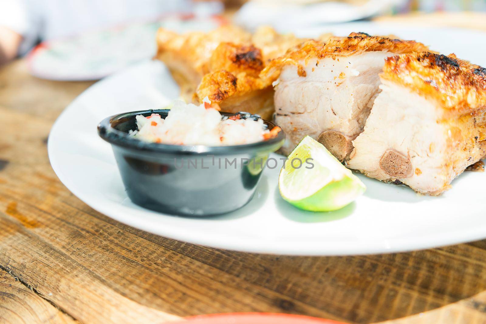 45 degree view of a plate of chicharron served with onion and lime on a plate on a wooden table by cfalvarez