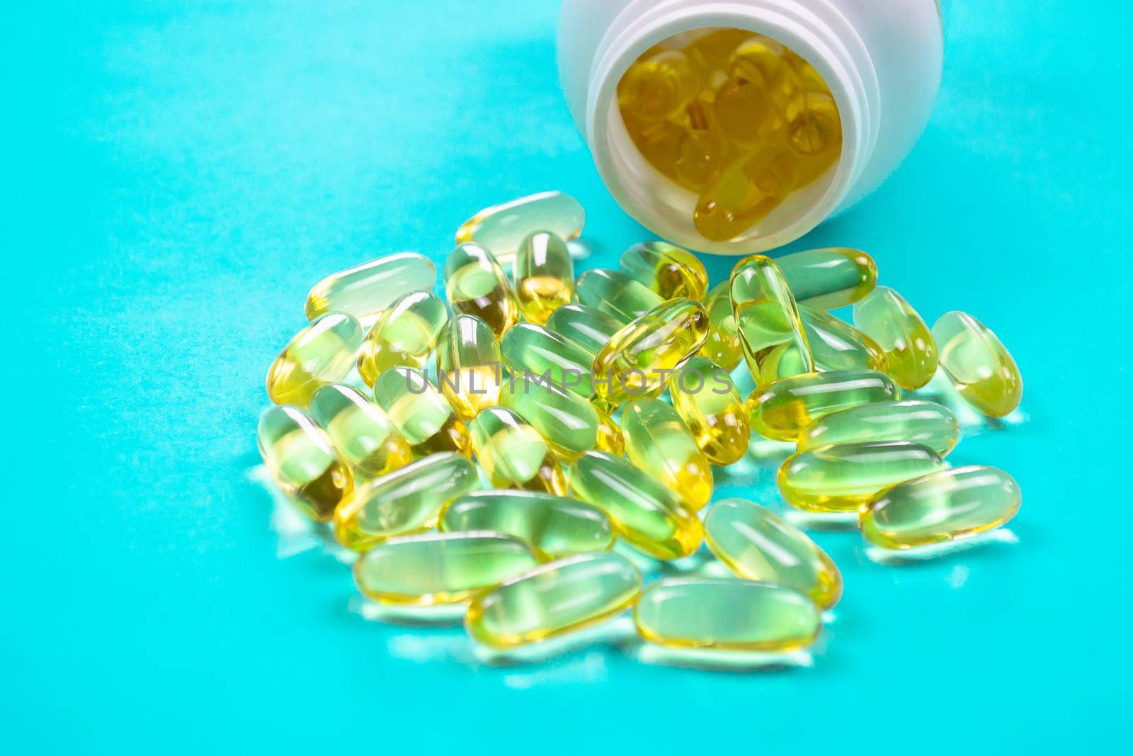 Omega 3 fish oil capsules spilling out of a bottle on a blue background.