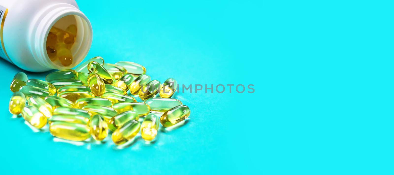 Omega 3 fish oil capsules spilling out of a bottle on a blue background.