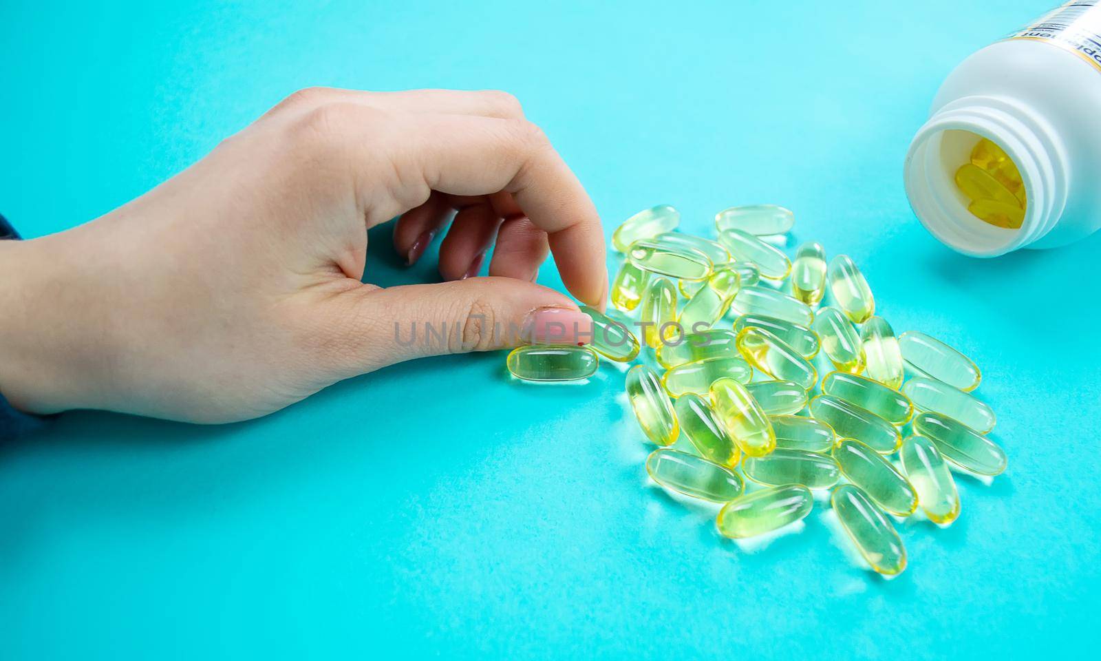 Omega 3 fish oil capsules spilling out of a bottle on a blue background.