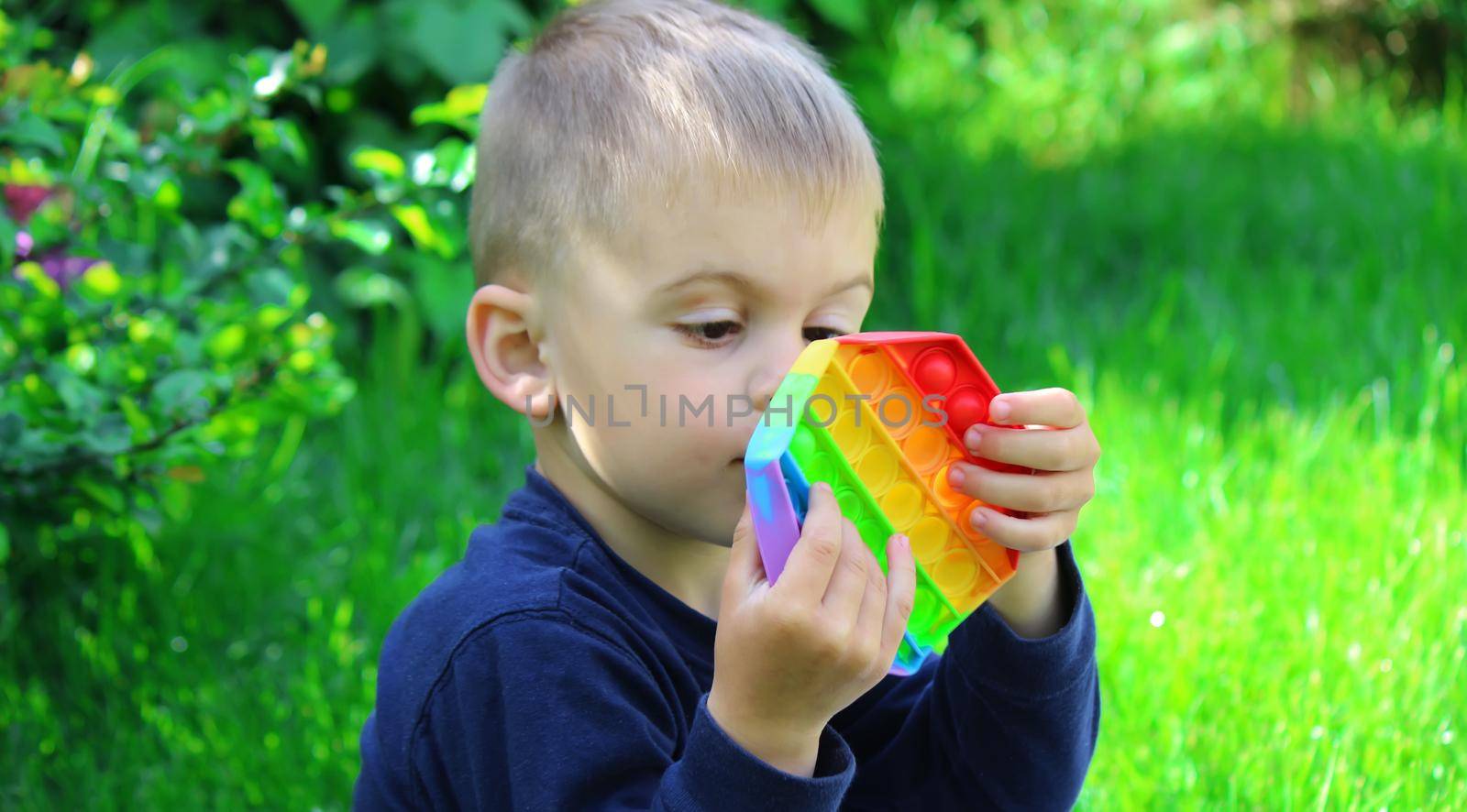 Pop it silicone anti-stress toy. The child plays on the grass. New trend Selective focus. Nature