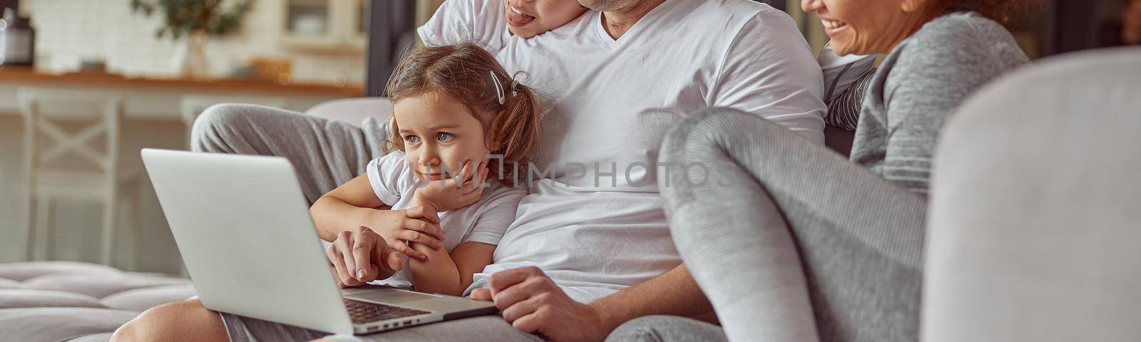 Joyful family watching video on notebook on couch by Yaroslav_astakhov