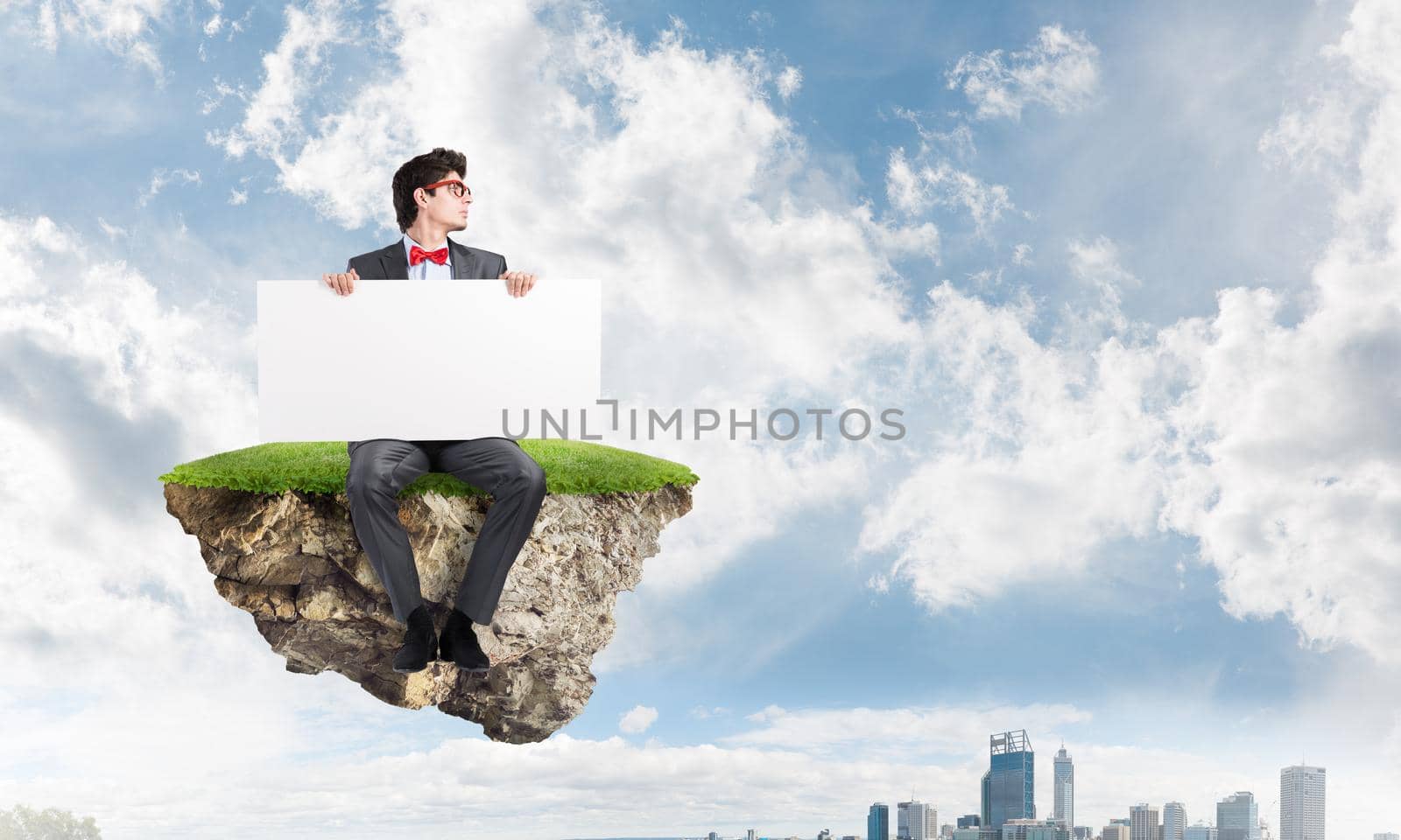 Young businessman with a clean banner on a flying island. Urban landscape in the background