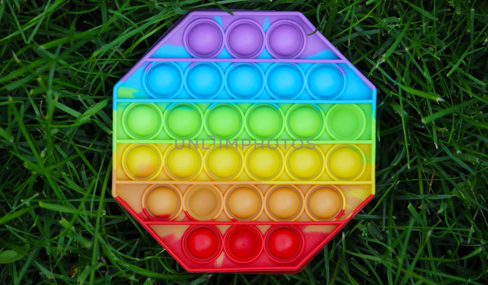 Pop it silicone anti-stress toy. The child plays on the grass. New trend Selective focus. Nature