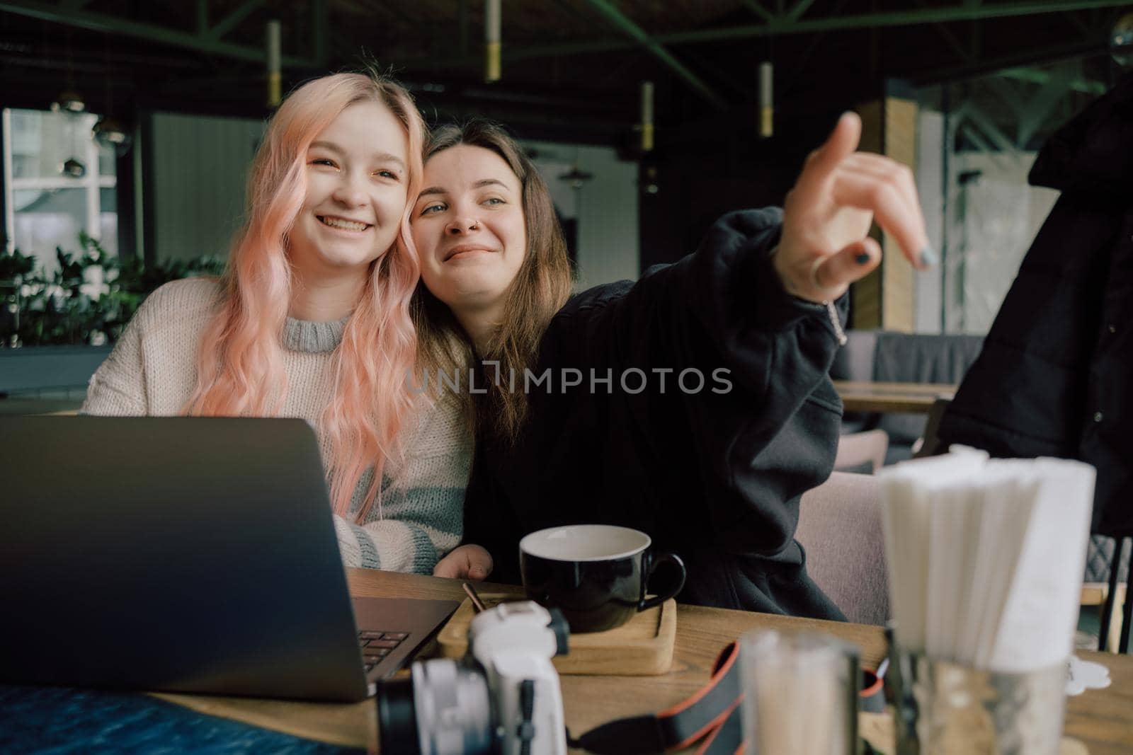 two happy young women sitting in coffee shop looking at laptop computer by Symonenko