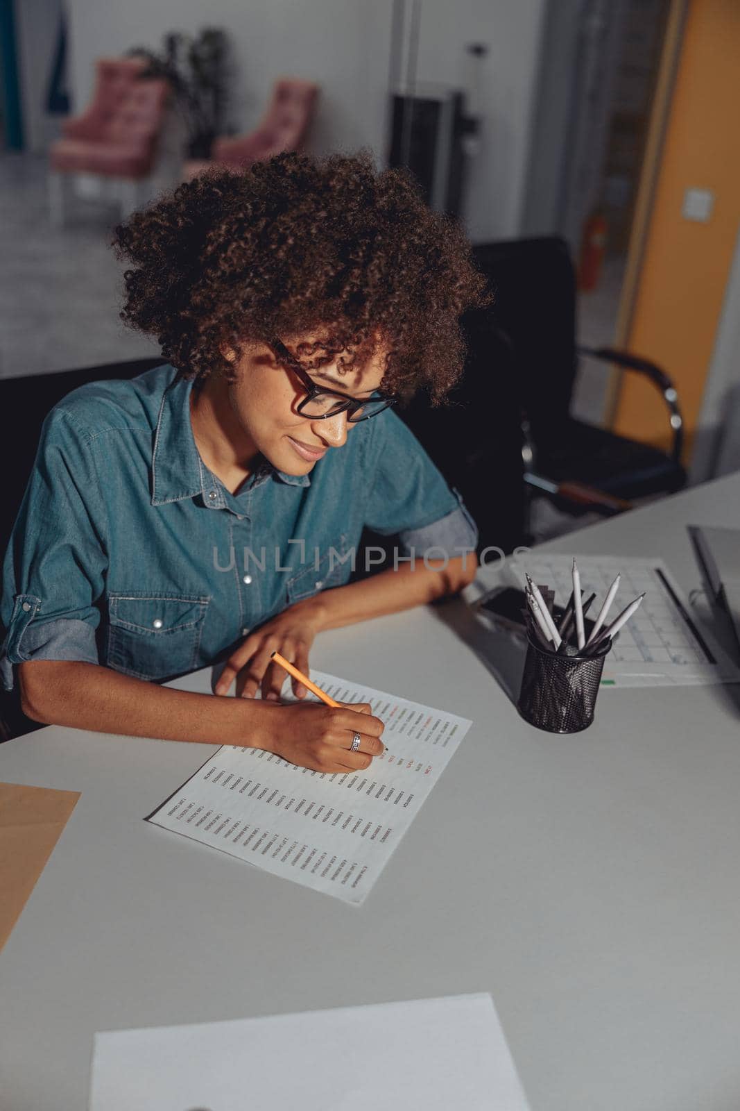 Top view of smiling African American woman working with document and sitting at workplace in the office