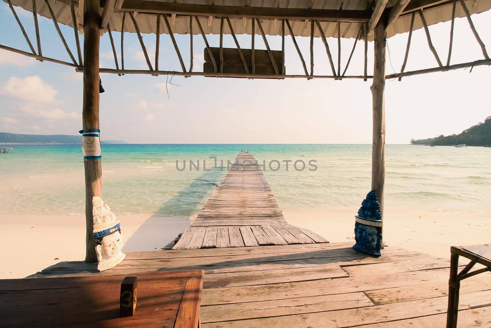 Scenic view from a gazebo of a wooden boardwalk leading to the white sandy beach of Koh Rong Samloen Island, a popular summer getaway destination in Cambodia