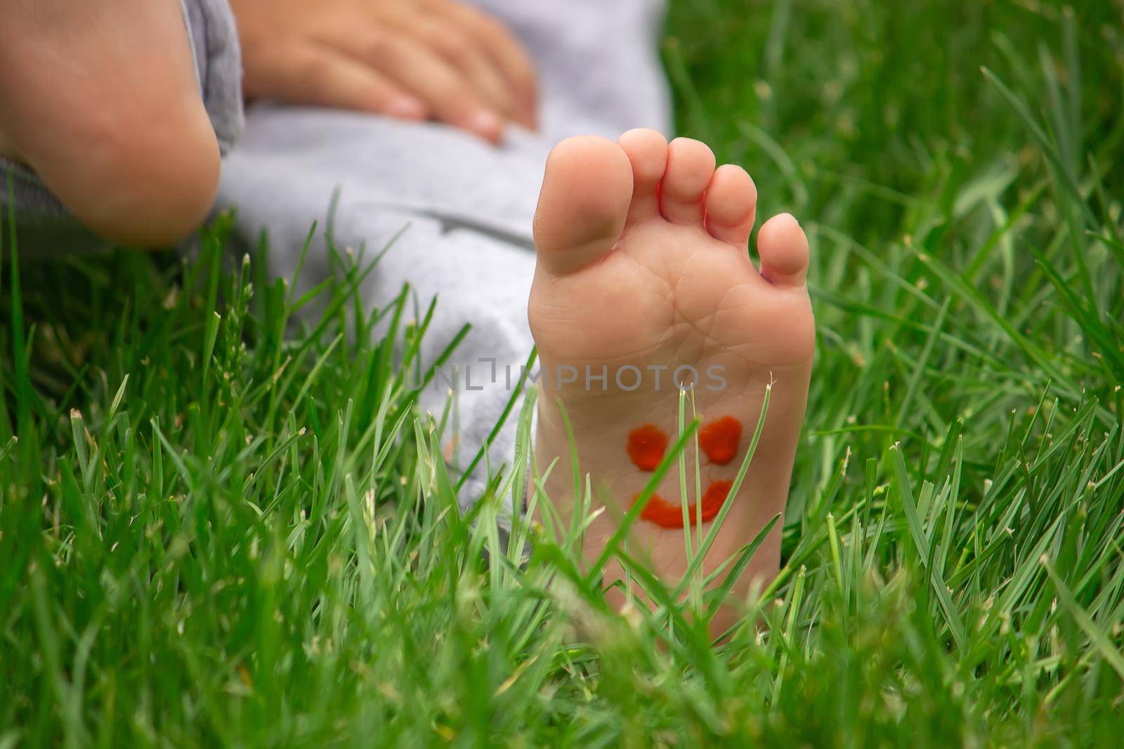child sitting on the grass, smiling on the child's leg with paints