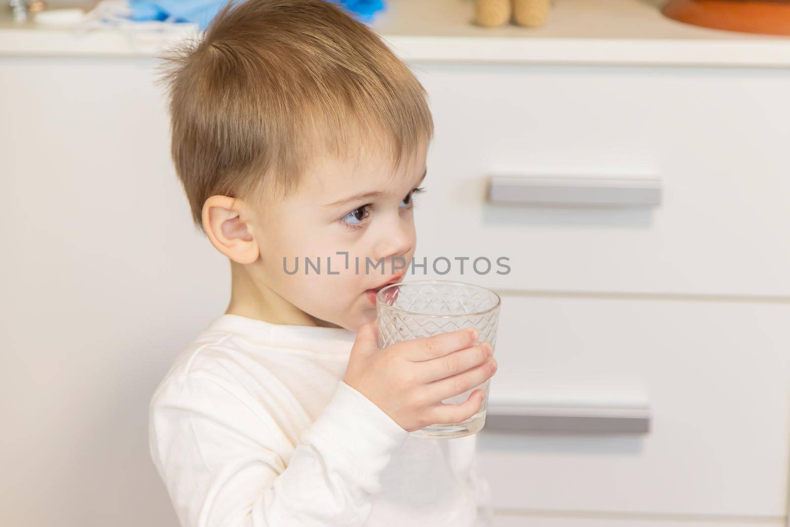 The child drinks water from a glass. Selective focus.
