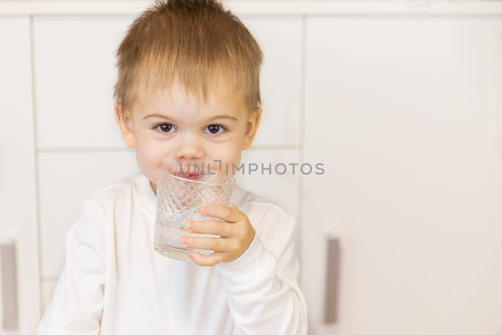 The child drinks water from a glass. Selective focus.