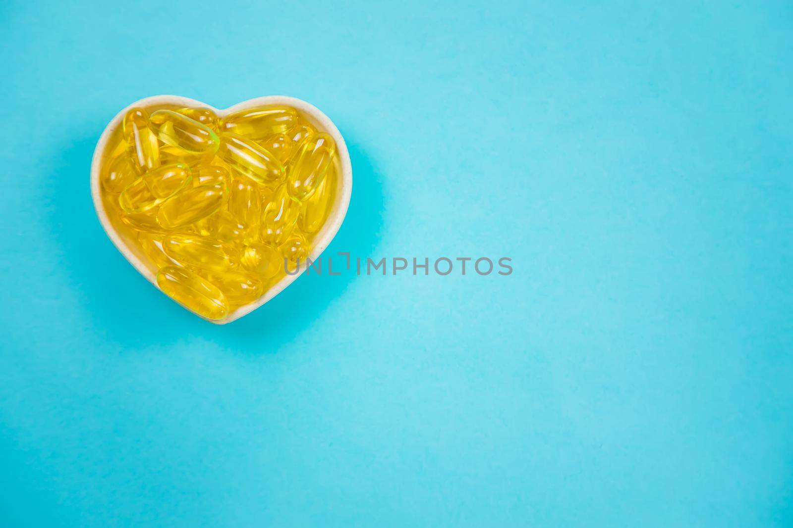 Omega 3 fish oil capsules spilling out of a bottle on a blue background.