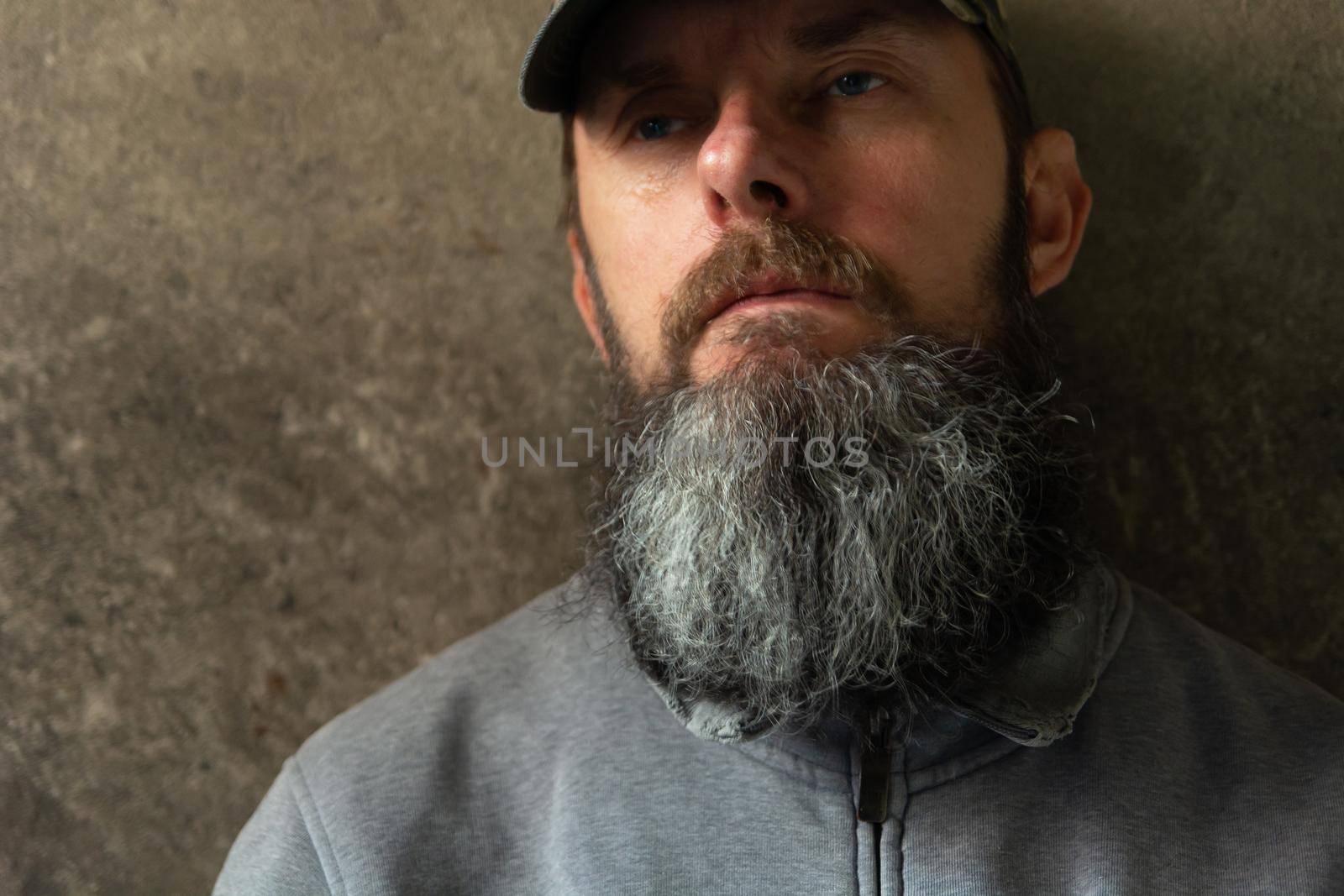 Bearded man in a baseball cap on the dark wall background