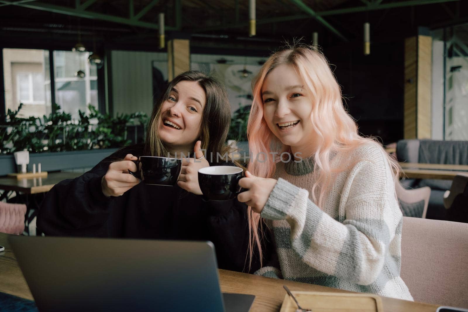 two happy young women sitting in coffee shop looking at laptop computer by Symonenko