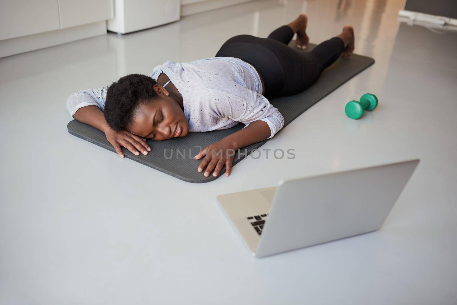 This workout really tires me out. Shot of a young woman looking exhausted while exercising at home. by YuriArcurs