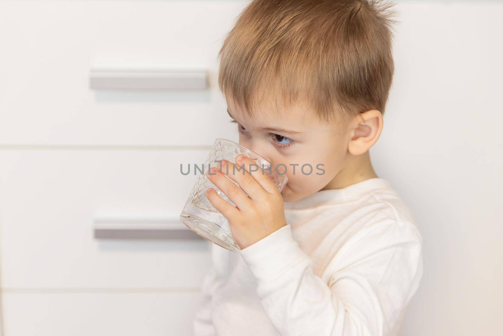 The child drinks water from a glass. Selective focus.