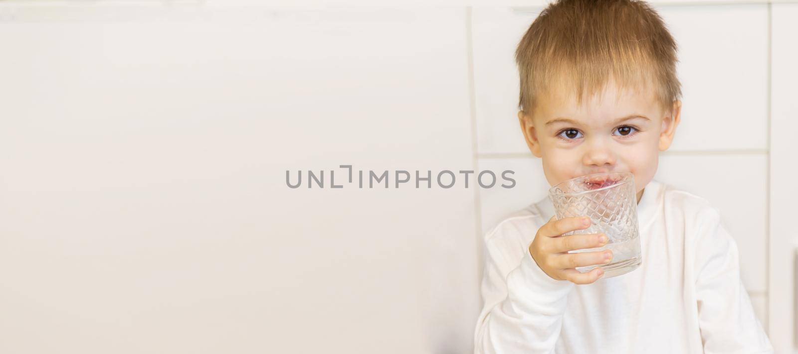 The child drinks water from a glass. Selective focus.