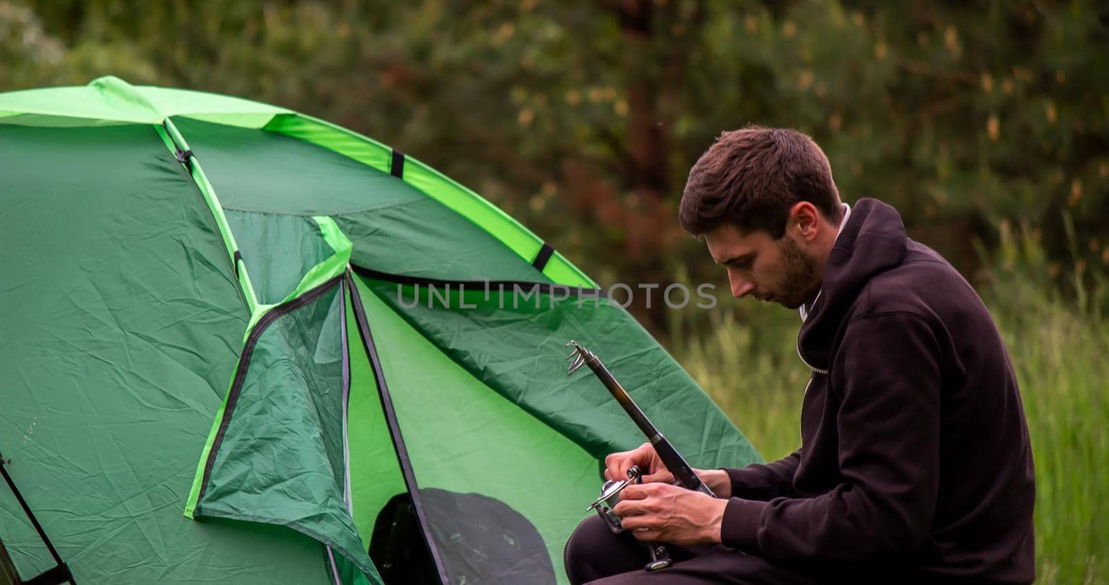 a man sits near a tourist tent. Nature, recreation, camping. Selective focus