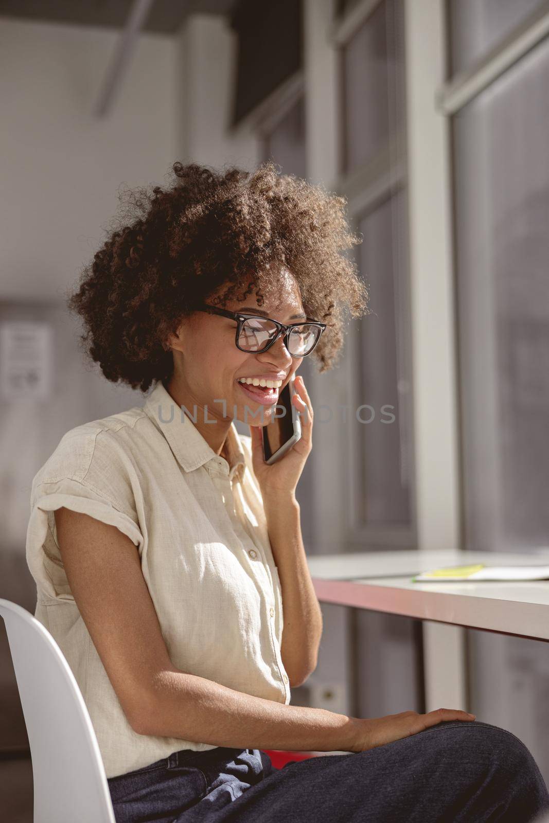 Pretty African American woman talking on her mobile phone and looking down while sitting at her work place