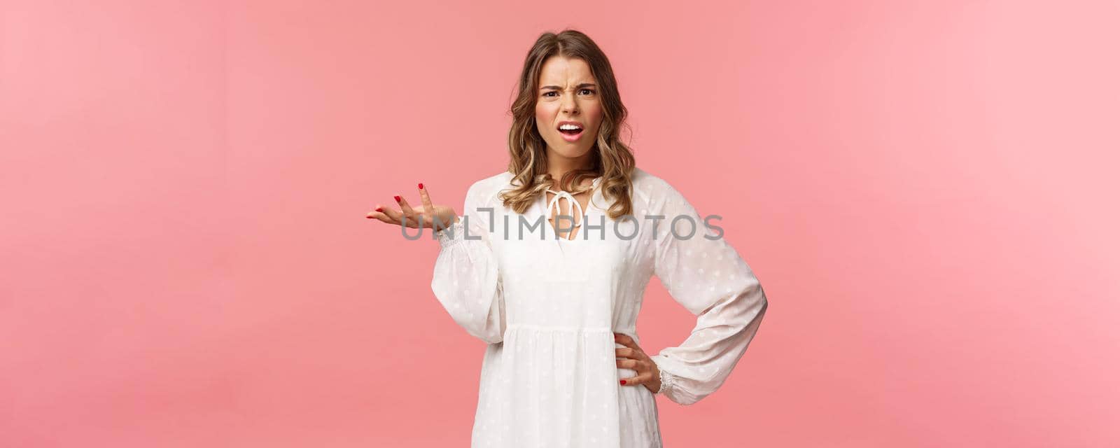 Whats your problem. Pissed-off and annoyed young blond girl looking questioned, cant understand what person complain about, raise on hand in dismay, shrug and grimace puzzled, pink background.