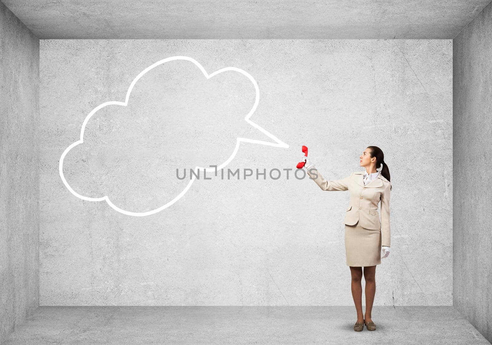 Young woman holding red phone and empty speech bubble on grey wall background. Call center operator in white business suit. Hotline telemarketing. Professional business assistance and consultation.