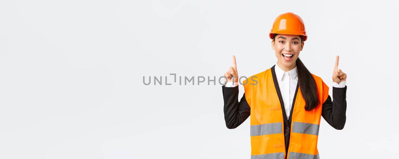 Building, construction and industrial concept. Happy smiling female asian engineer in safety helmet and reflective clothing, introduce new object, estate for sale. Architect pointing fingers up by Benzoix