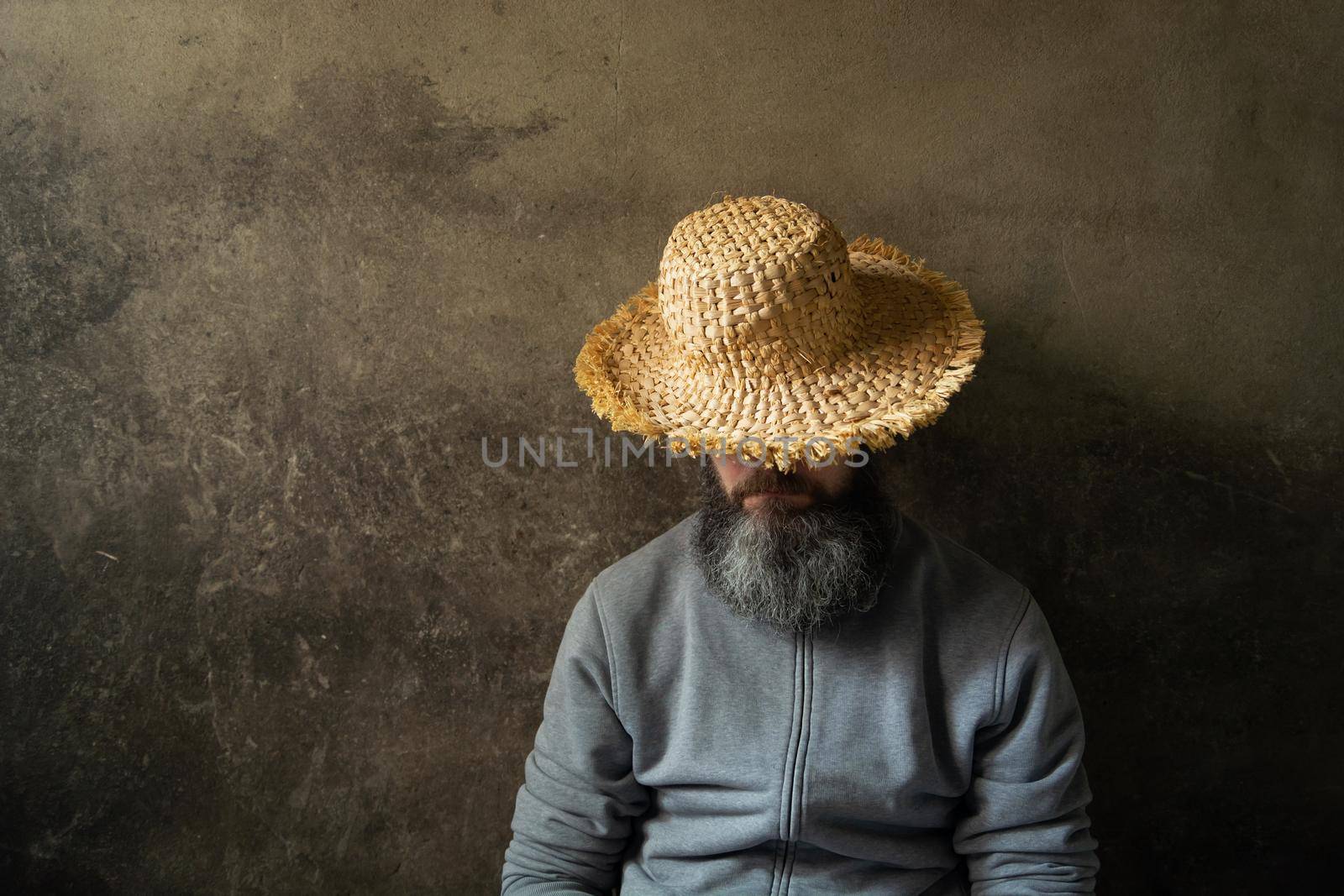 A napping man with a beard in a hat against the background of a dark wall