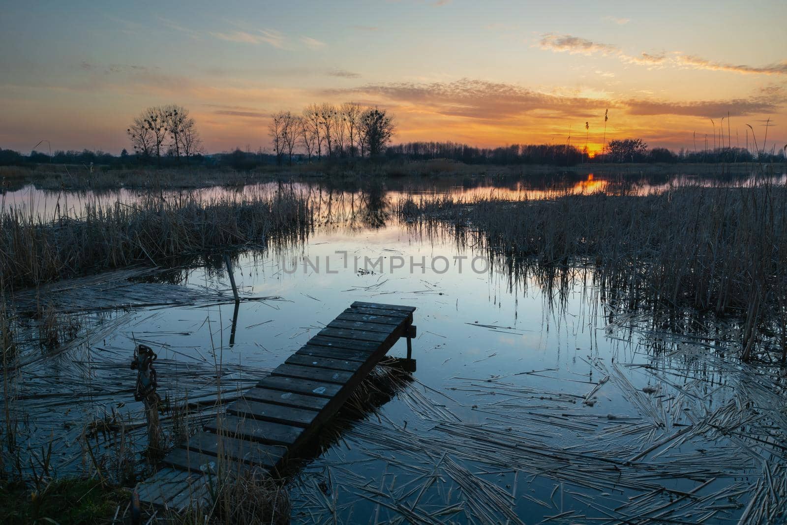 Footbridge on the shore of the calm lake and sunset view