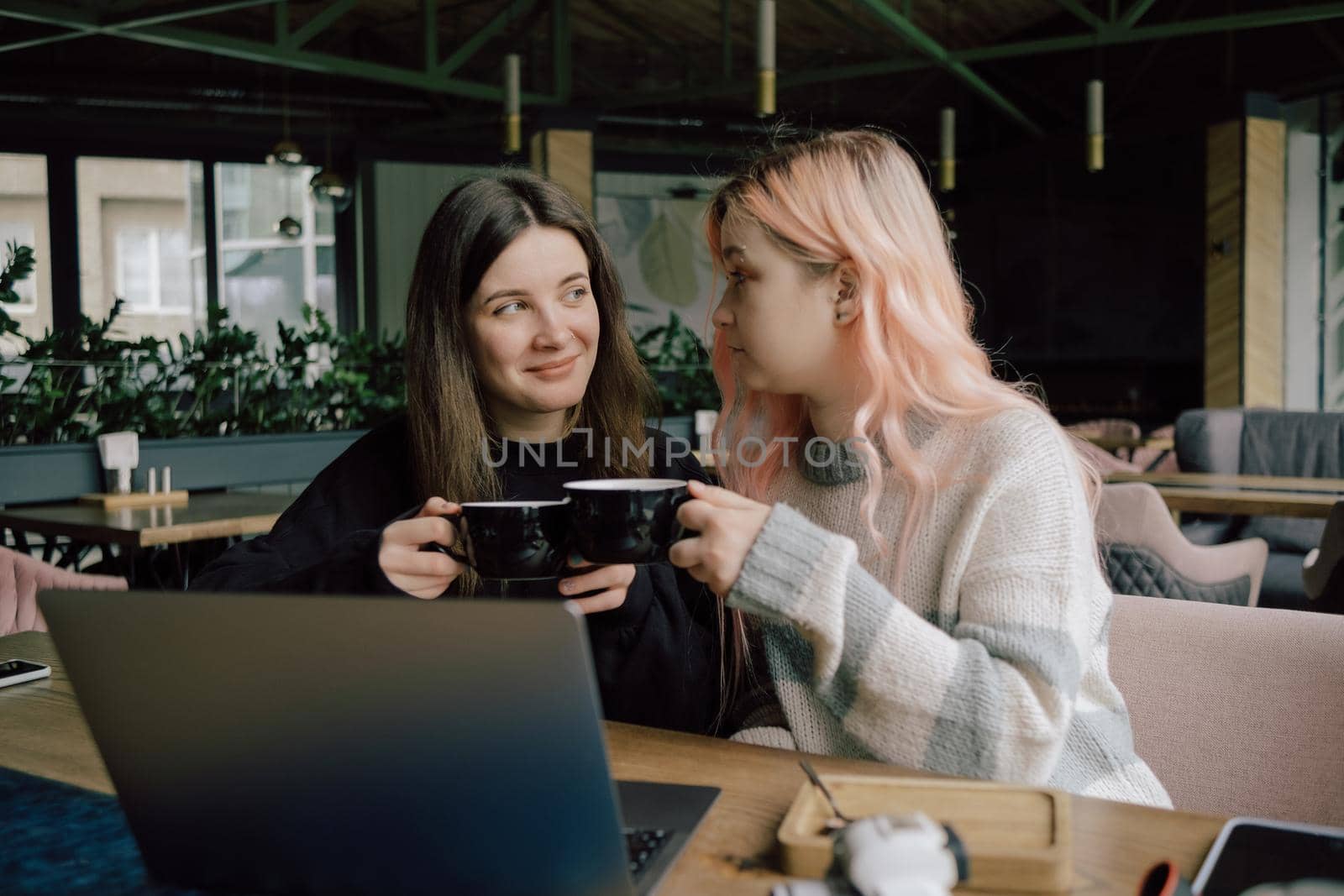 two happy young women sitting in coffee shop looking at laptop computer by Symonenko
