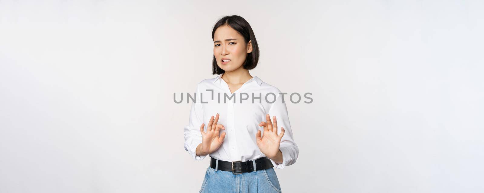 No thank you. Young disgusted asian woman declining proposal, shaking hands and step back, looking with dislike, rejecting offer, standing over white background by Benzoix