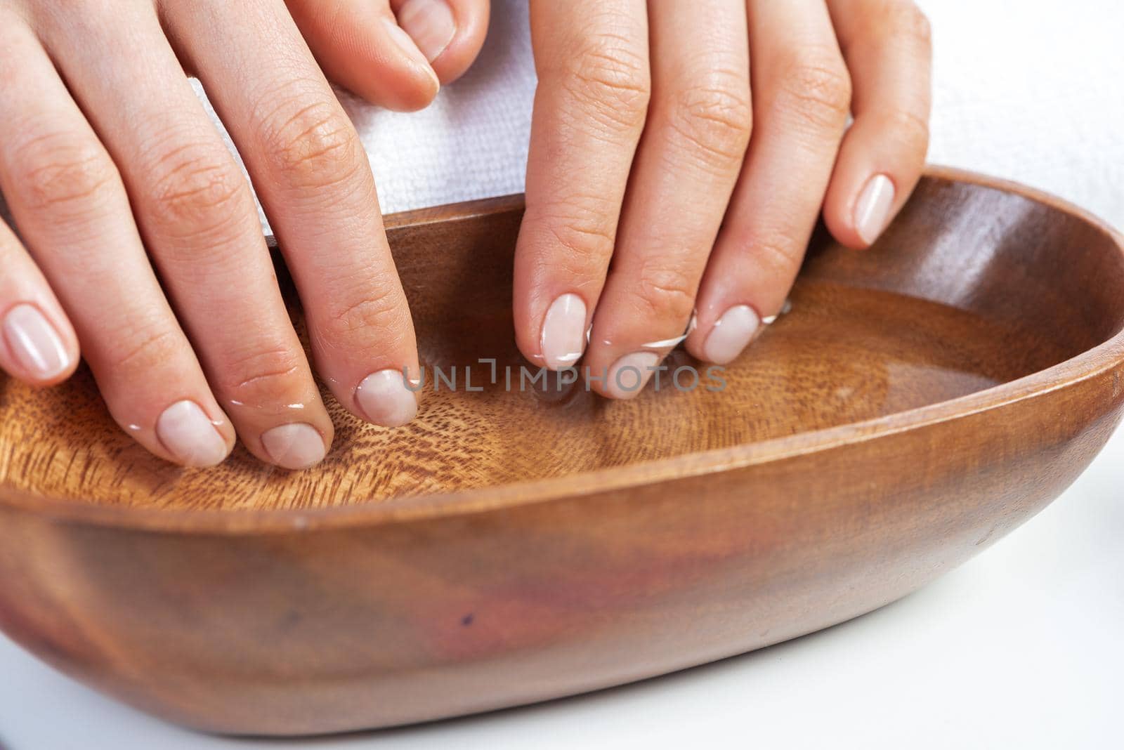 Closeup female hands in wooden bowl with water. Spa procedure and relaxation. Female hands preparing for manicure. Professional nail care and beautician service. Beauty and hygiene concept