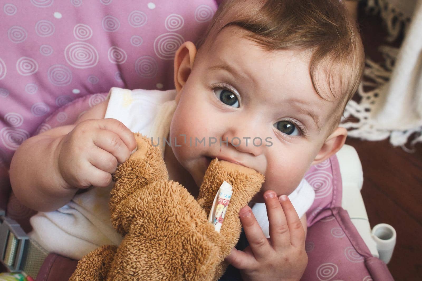 Cute baby girl playing with her brown teddy bear soft toy and chewing on the bear's foot
