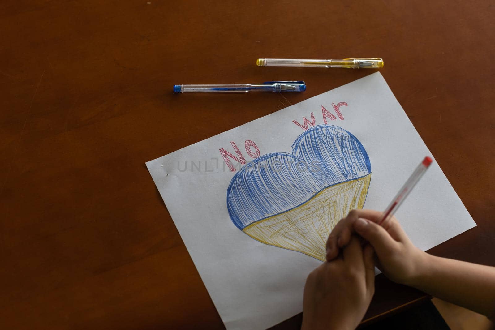 children's drawing, flags of ukraine are drawn on a sheet, children's hands hold a heart made, war between countries, peace concept.