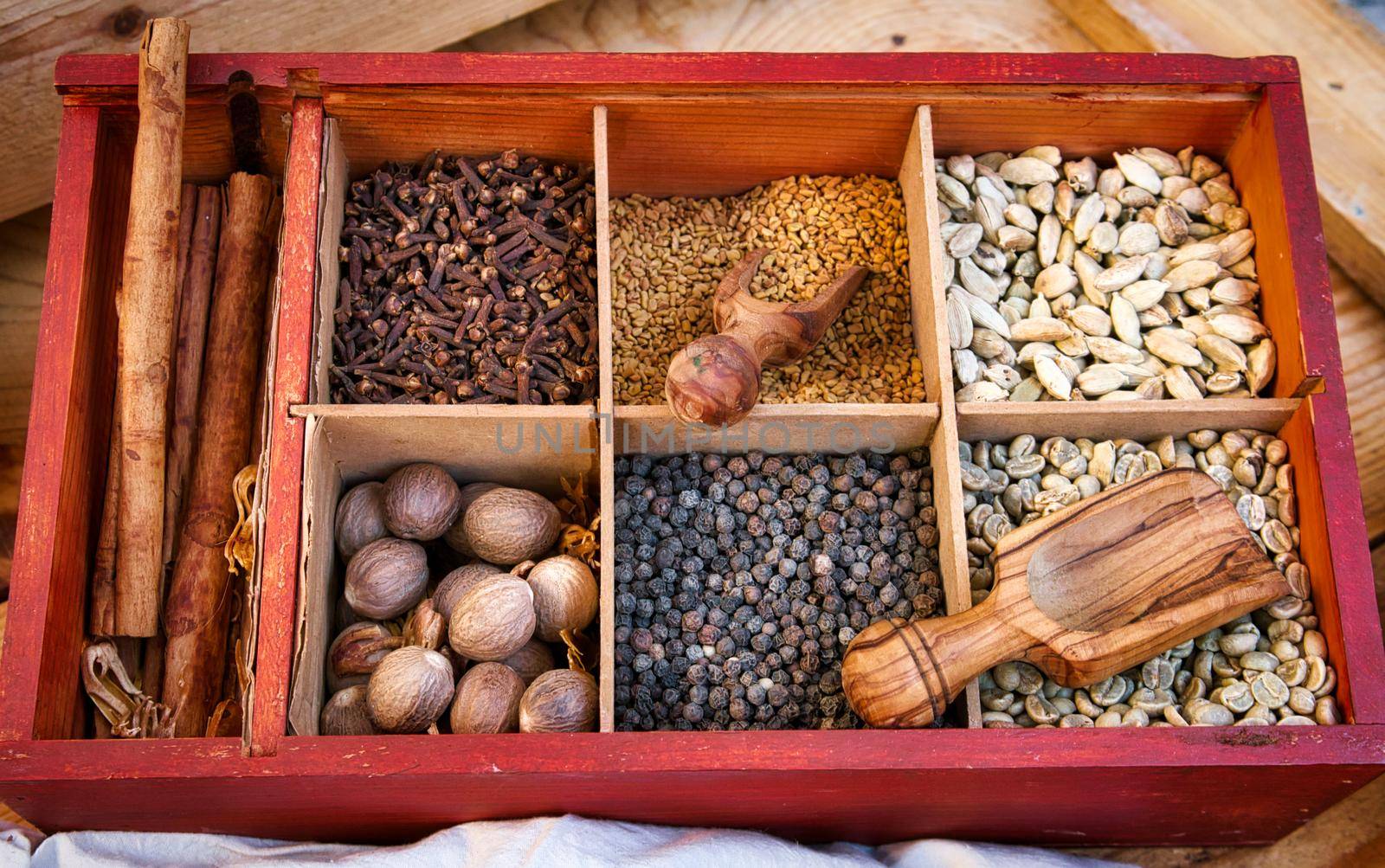 Various spices and condiments in boxed compartments used in eastern cooking with wooden serving spoons