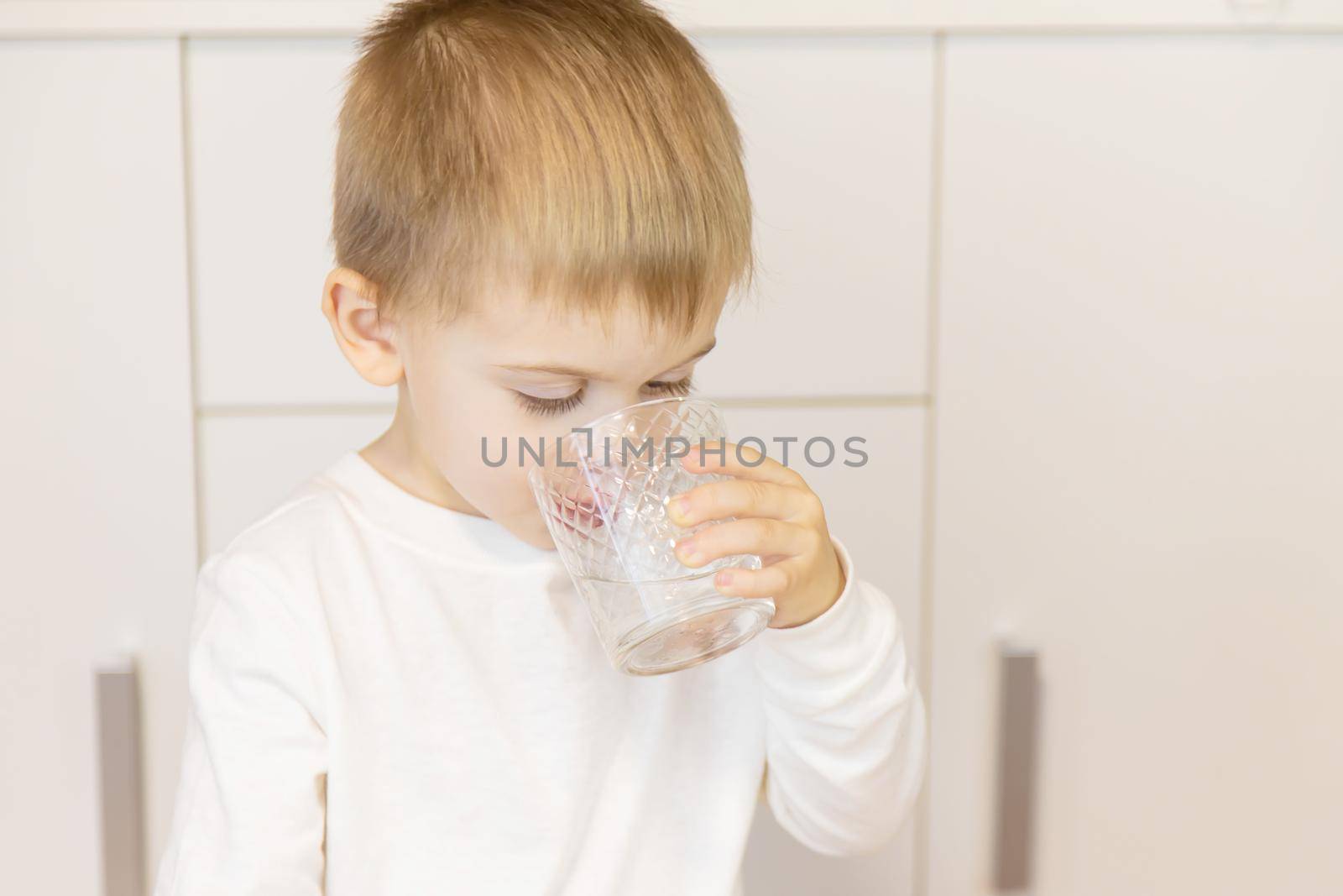 The child drinks water from a glass. Selective focus.