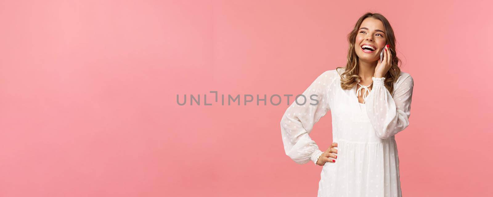 Portrait of carefree good-looking girl with blond short hair, wear white dress, laughing happy as talking on phone, hear funny joke, have conversation using mobile, hold smartphone and chuckle.