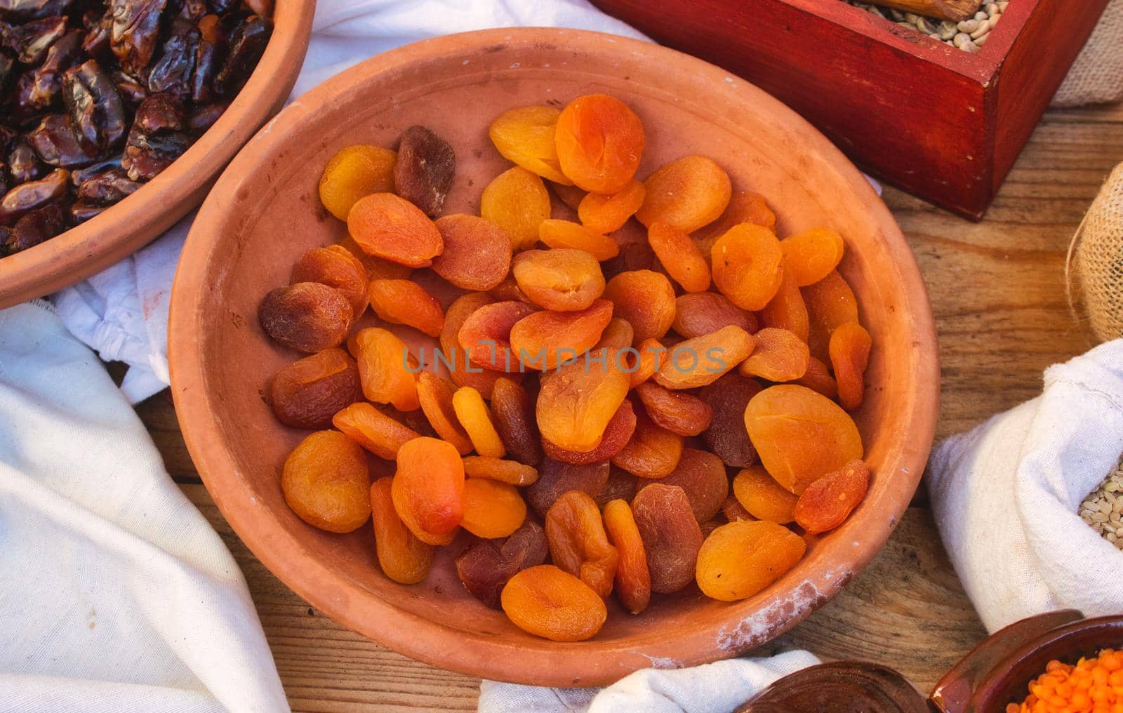 Dried apricots in a terracotta bowl on a wooden table at an outdoor food market stall