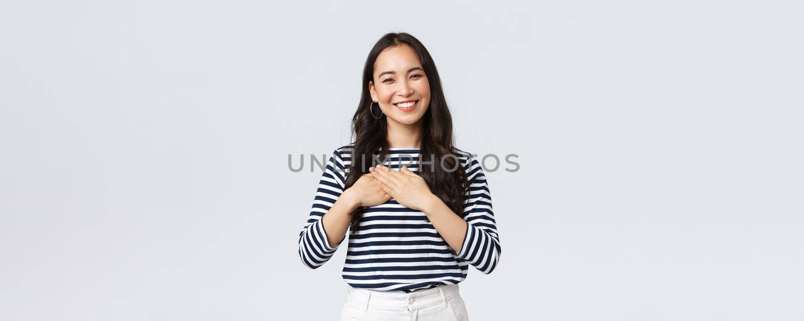 Lifestyle, people emotions and casual concept. Touched tender smiling asian woman gladly receive praises, hold hands on heart and grinning thankful, appreciate compliment by Benzoix