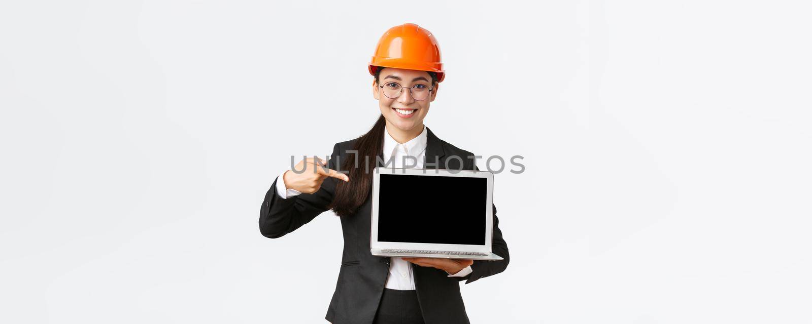 Smiling pleased asian female chief engineer showing chart with enterprise profit, making presentation during investors meeting, wearing safety helmet, pointing at laptop screen, white background by Benzoix