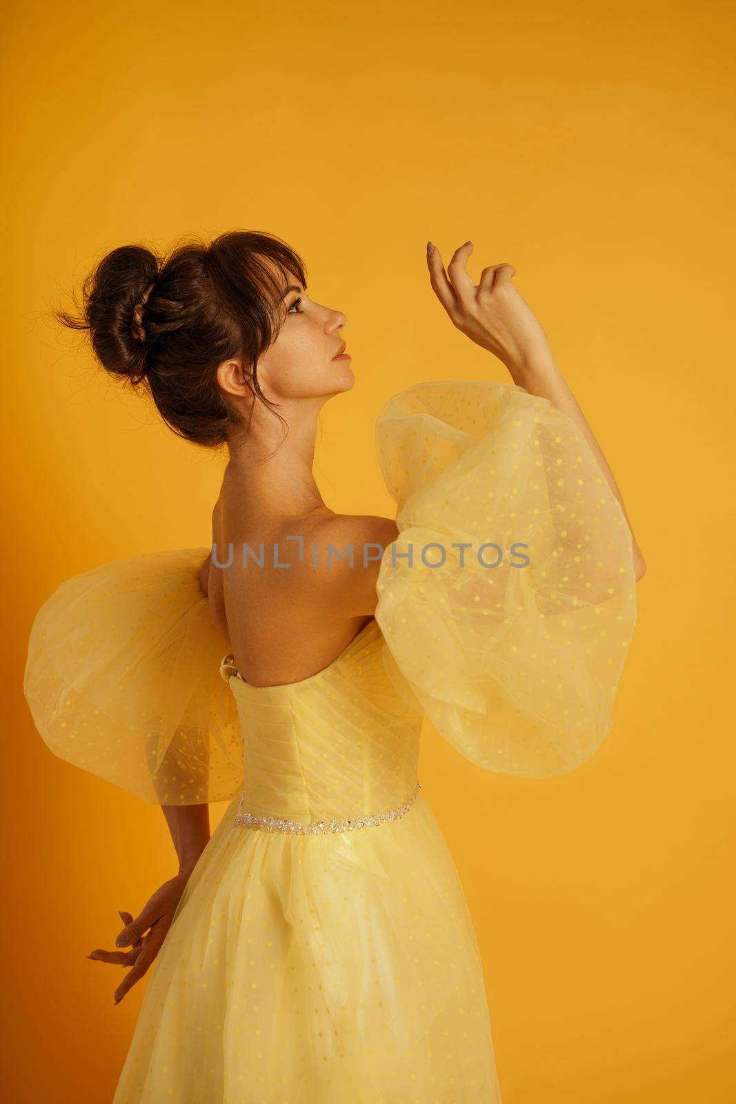 Profile portrait of a beautiful middle-aged woman in a yellow dress, her hair pulled up against a yellow background.