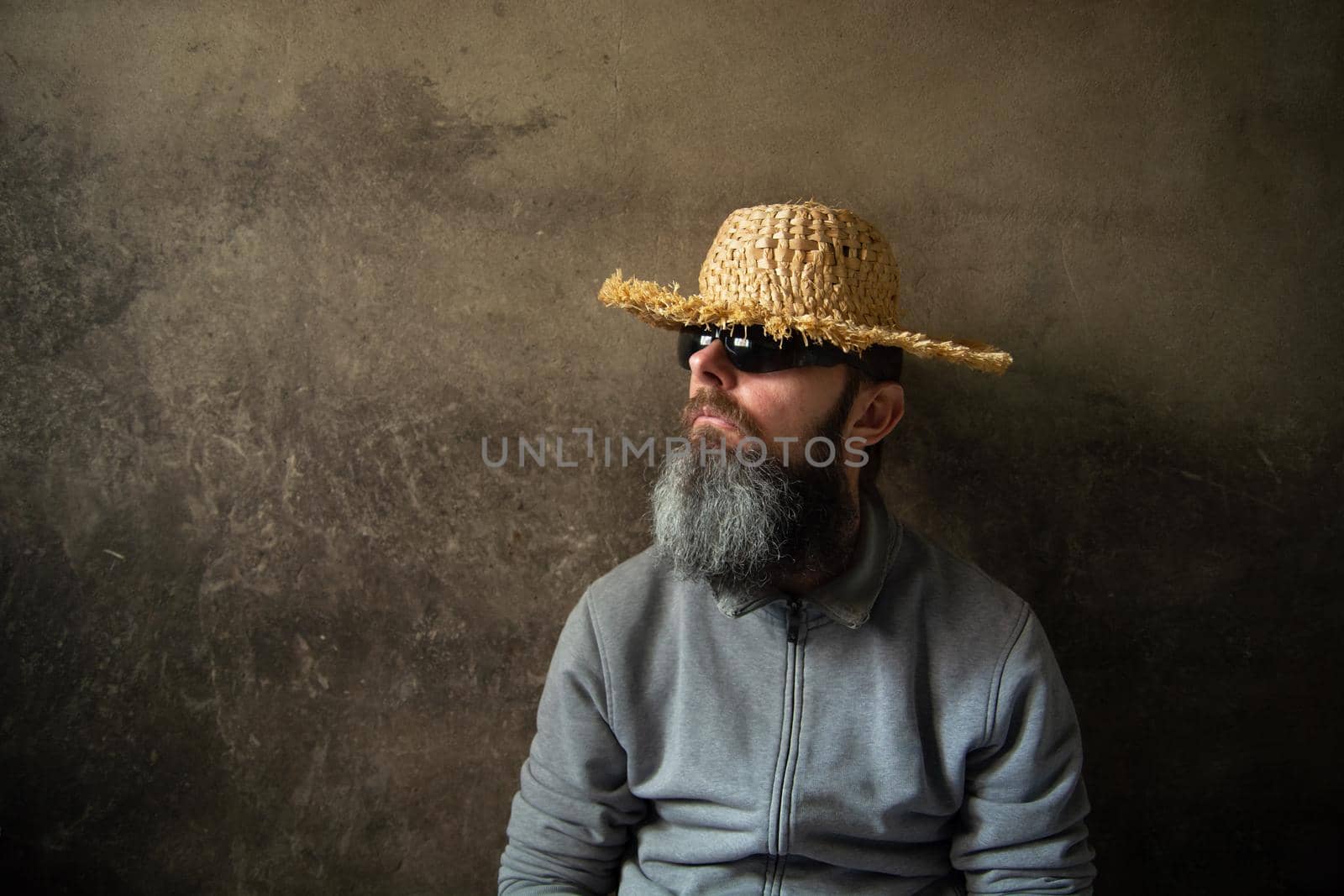 A man with a beard in a straw hat against a wall background