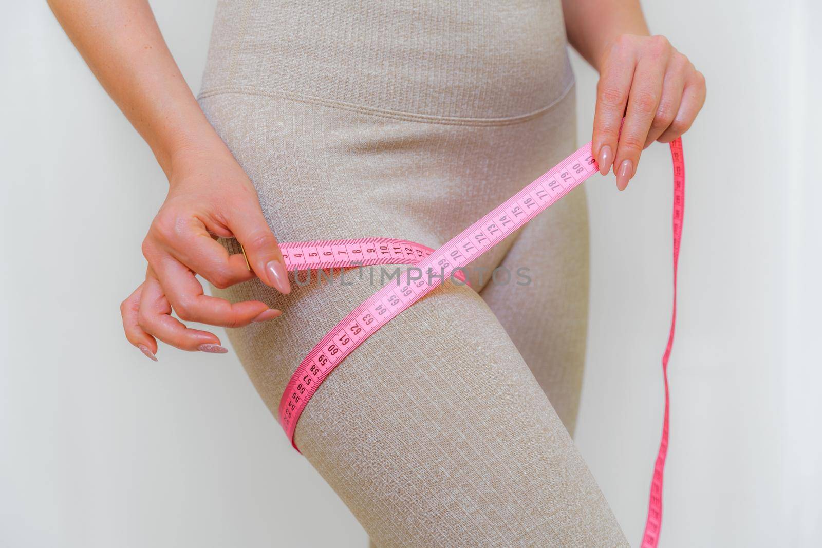 Cropped view of slim woman measuring her leg with tape measure at home, close-up. An unrecognizable European woman checks the result of a weight loss diet or liposuction indoors. Healthy lifestyle. by Matiunina