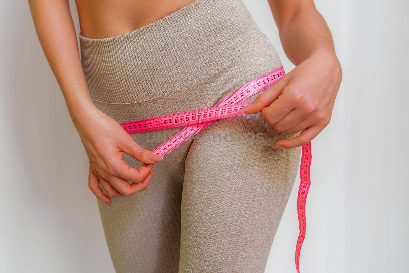 Cropped view of slim woman measuring hips with tape measure at home, close up. An unrecognizable European woman checks the result of a weight loss diet or liposuction indoors. Healthy lifestyle. by Matiunina
