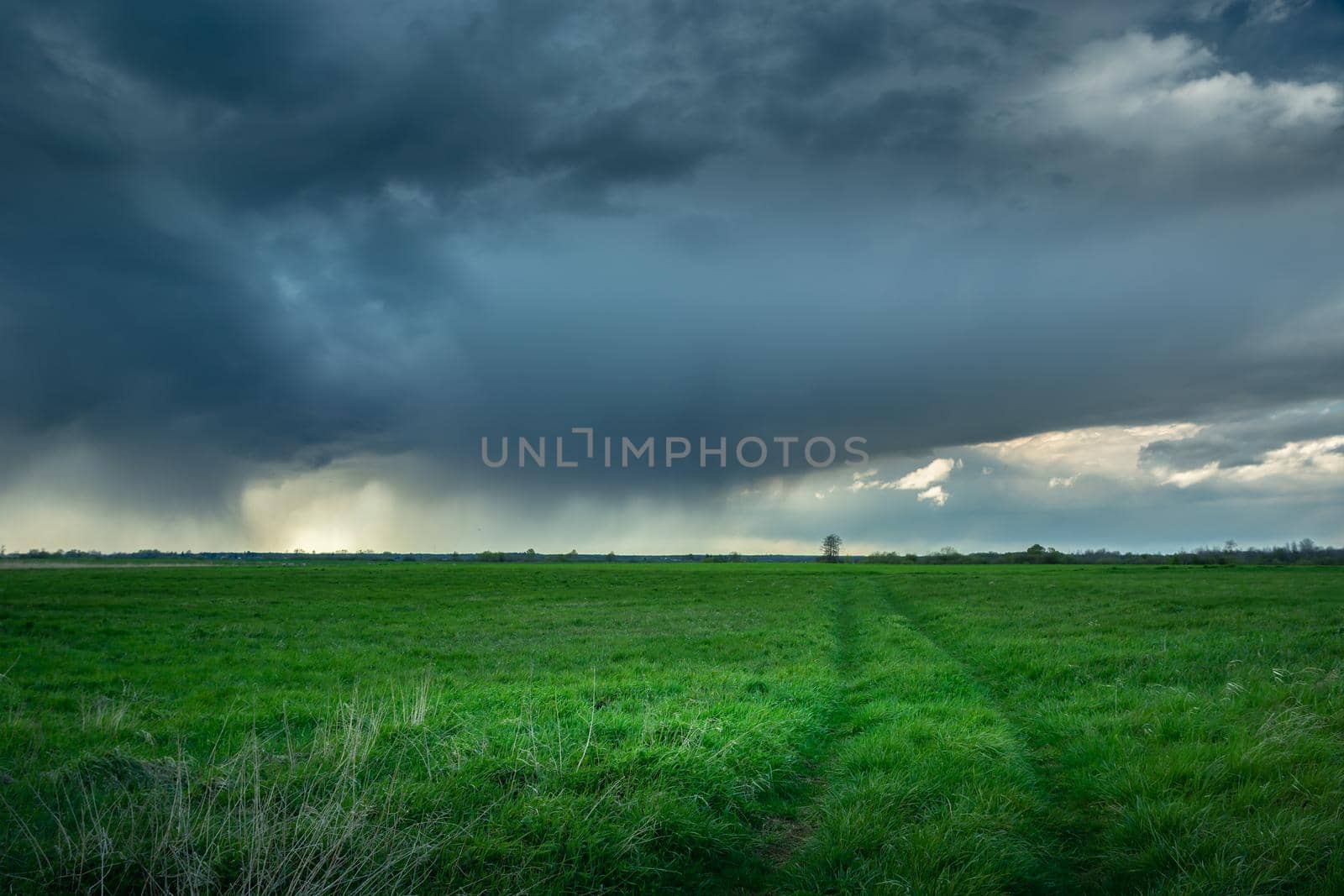 The road through the meadow and the rainy dark cloud, spring day