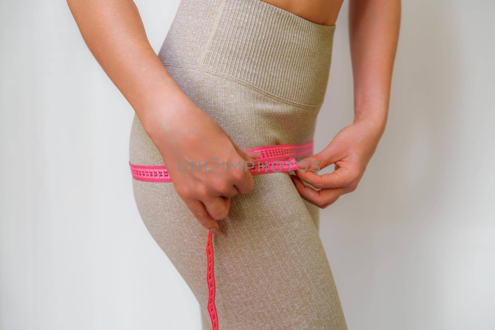 Cropped view of slim woman measuring hips with tape measure at home, close up. An unrecognizable European woman checks the result of a weight loss diet or liposuction indoors. Healthy lifestyle. by Matiunina