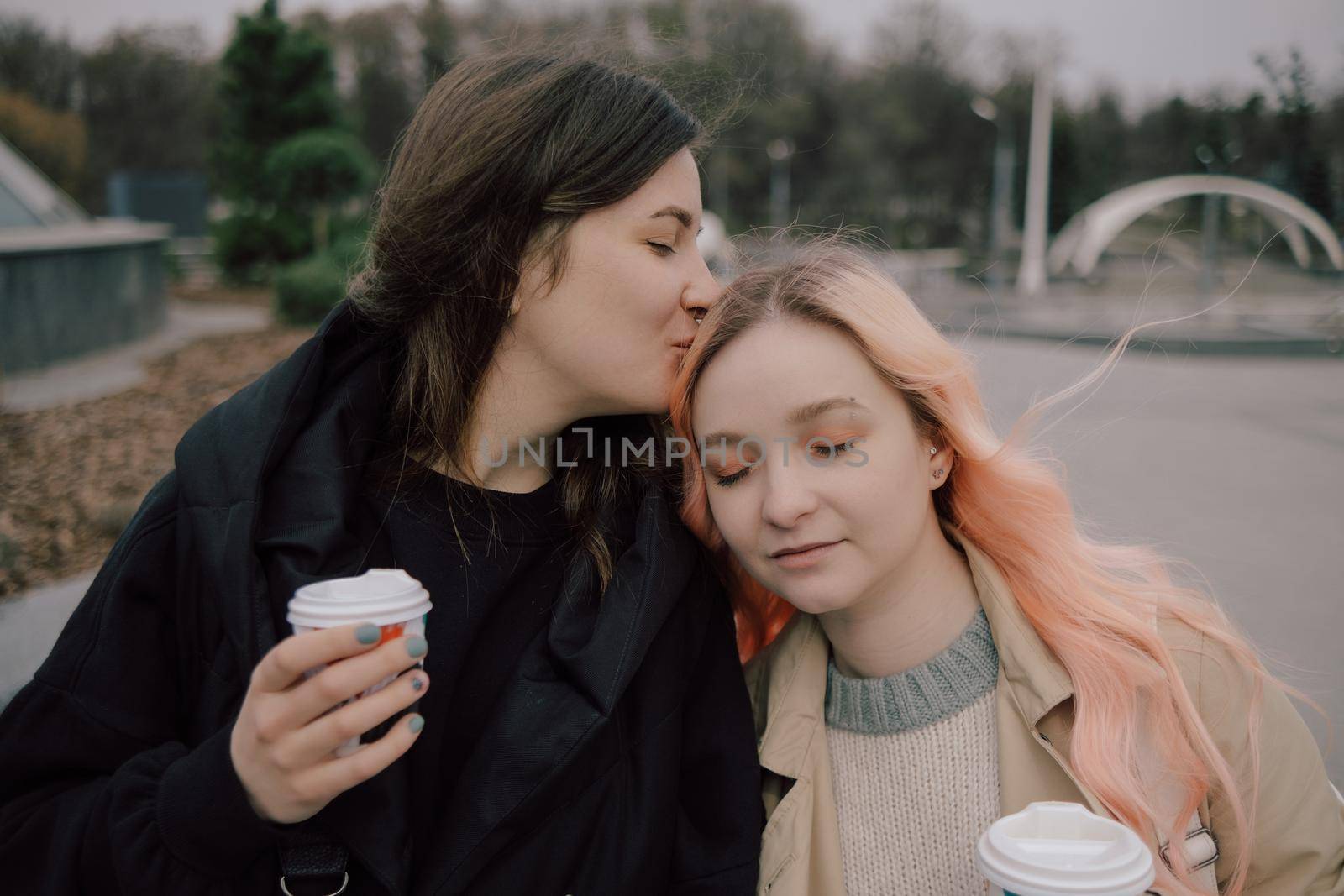 Young ukrainian lesbian couple kissing each other at the street with coffee pink hair