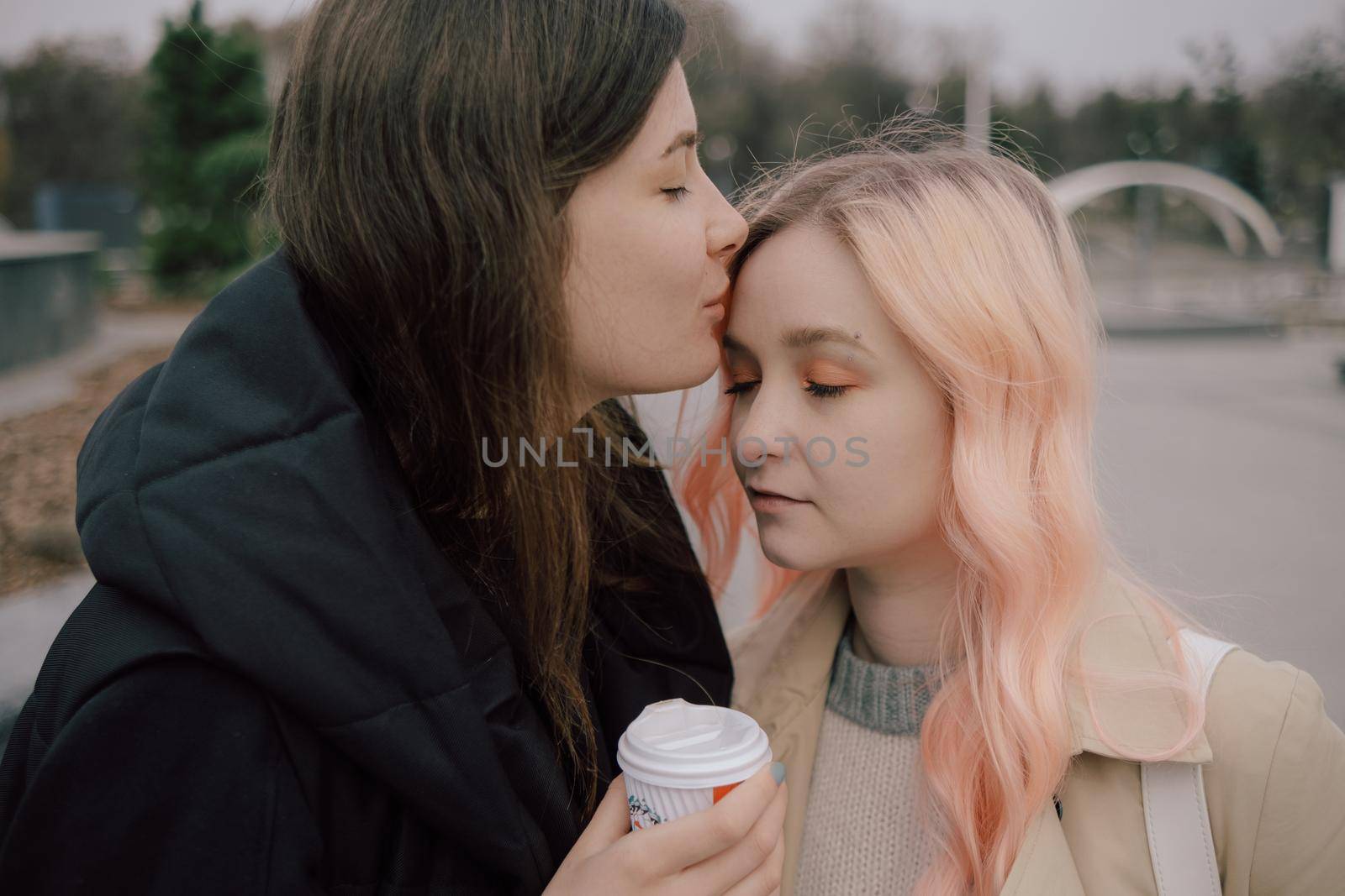 Young ukrainian lesbian couple kissing each other at the street with coffee pink hair