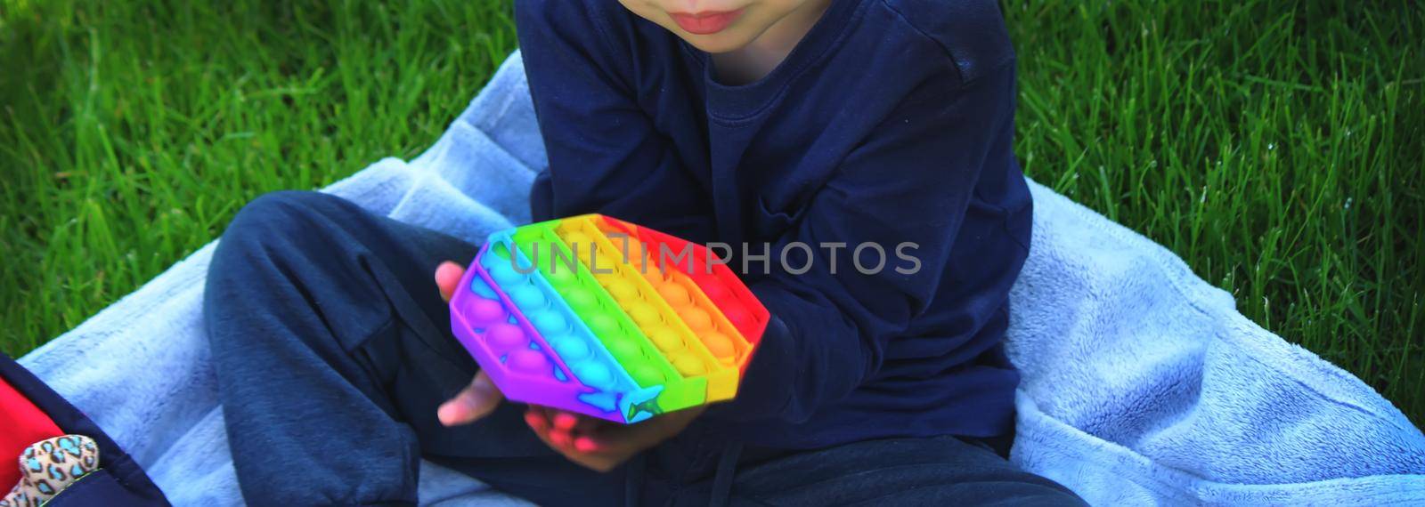 Pop it silicone anti-stress toy. The child plays on the grass. New trend Selective focus. Nature
