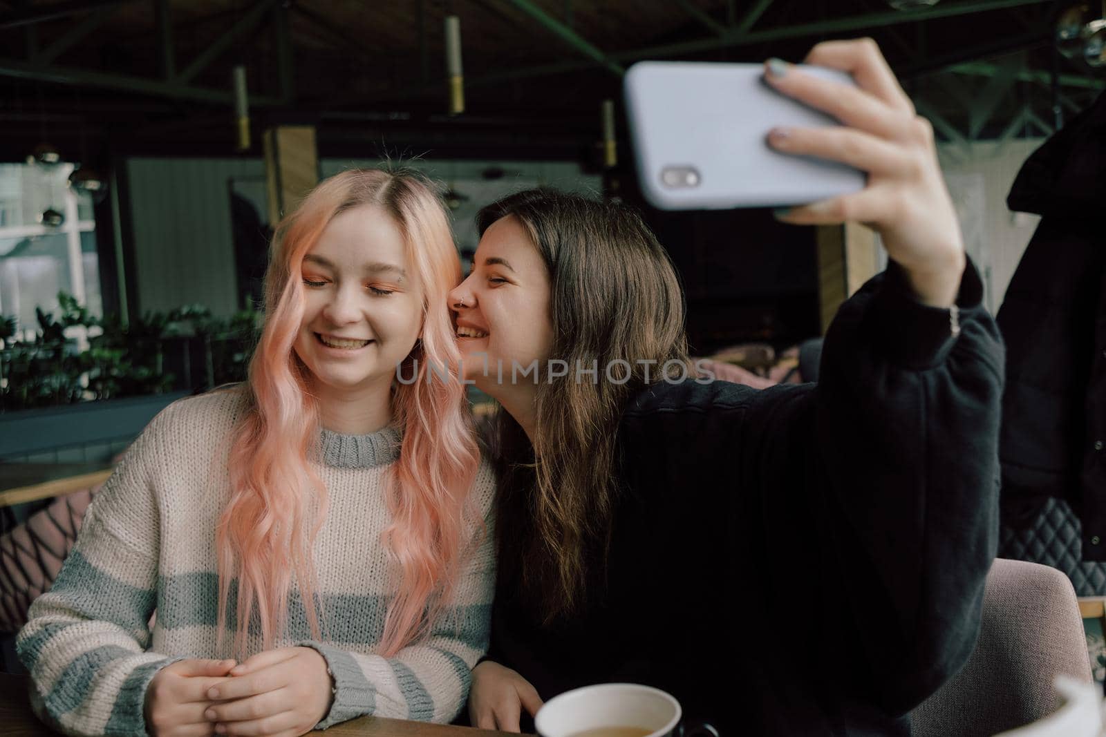 Cheerful young lesbian couple selfie using mobile phone at a coffee shop. Two joyful attractive Asian girls together at restaurant or cafe. by Symonenko