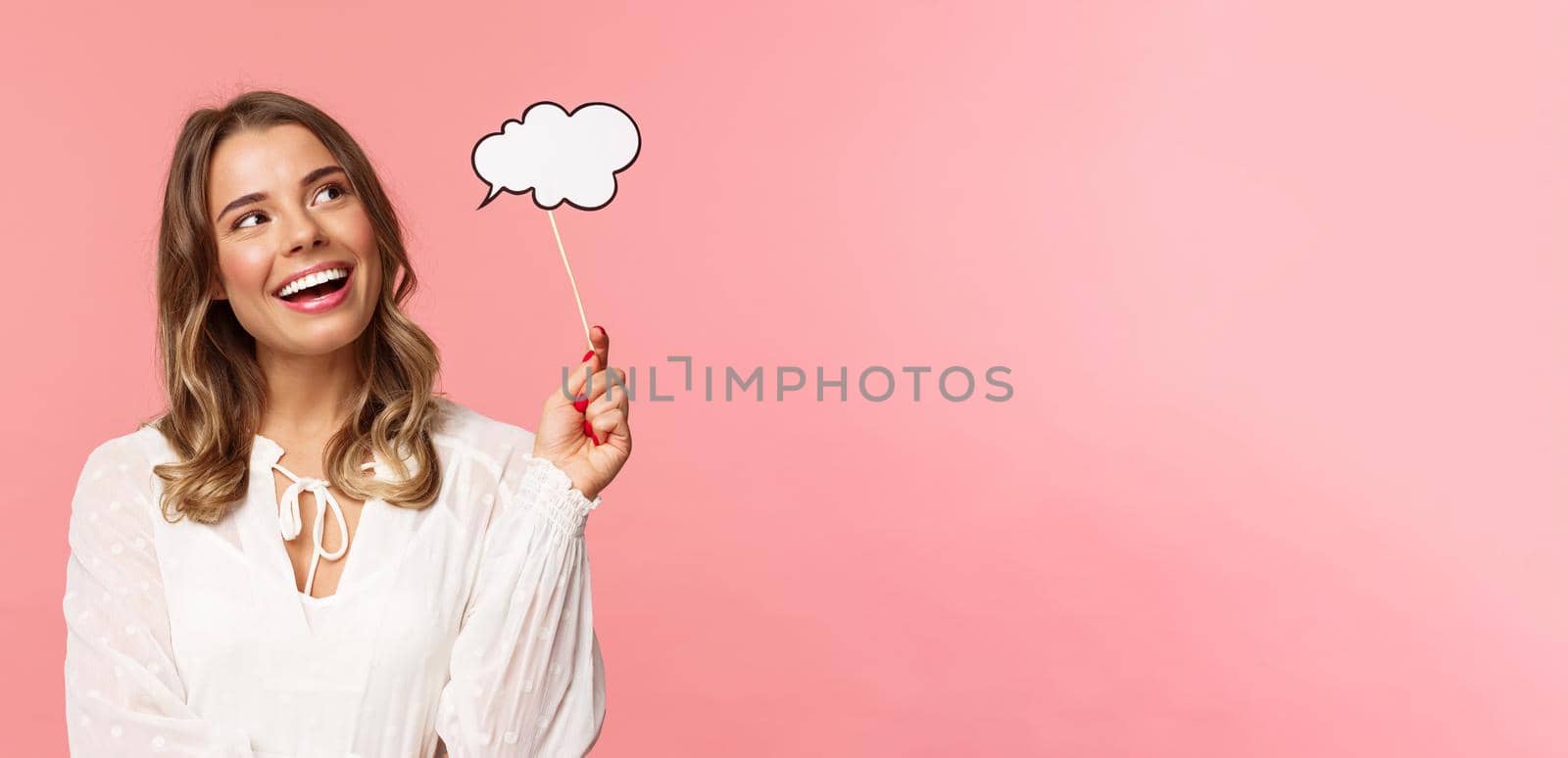 Spring, happiness and celebration concept. Dreamy and lovely blond girl daydreaming, saying something, holding comment cloud stick near mouth as if talking, look away daydreaming.